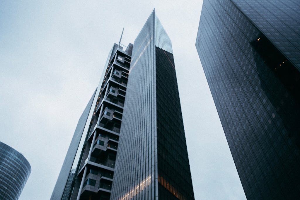 Low angle view of towering modern skyscrapers with glass facades under an overcast sky.